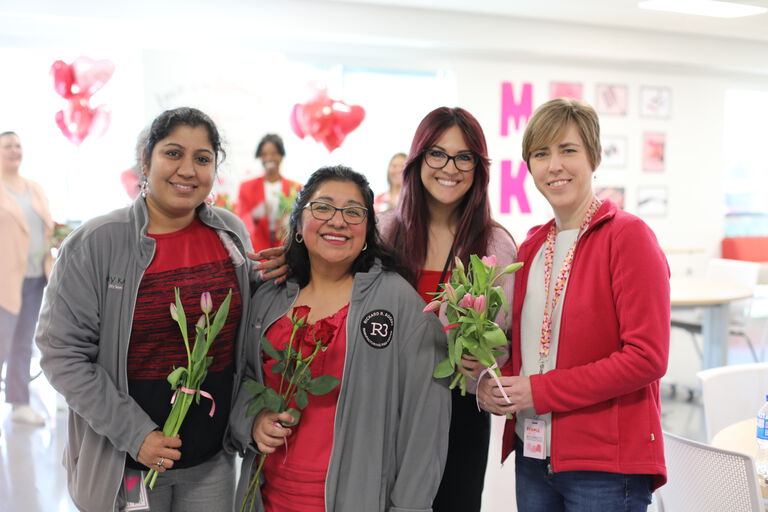 Group of people holding flowers during an indoor event with heart-shaped balloons in background