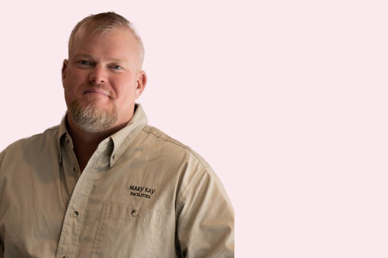 Person wearing a beige Mary Kay branded button-up shirt against a light pink background