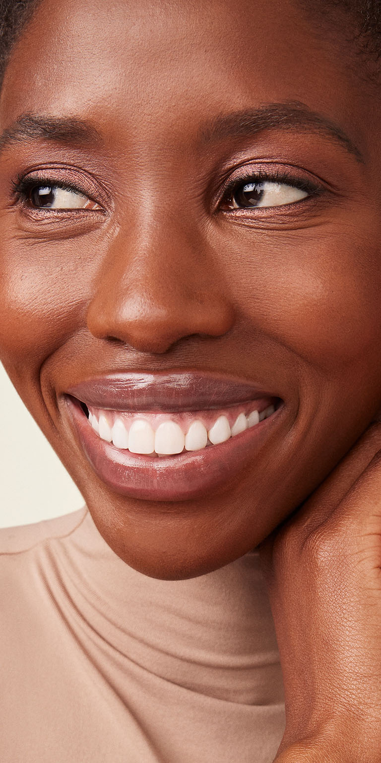 Model with deep skin tone smiling to the side of the camera
