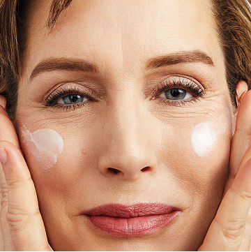 Woman smiling at the camera putting Mary Kay Vitamin C+E Serum on both cheeks